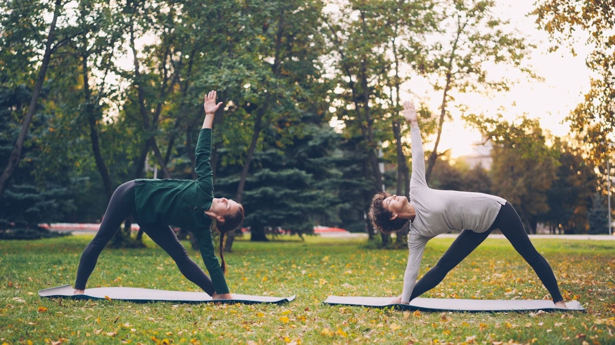 Pretty women is trendy sports clothing are training outdoors doing yoga enjoying movement, fresh air and warm autumn weather. Sports, leisure and youth concept.